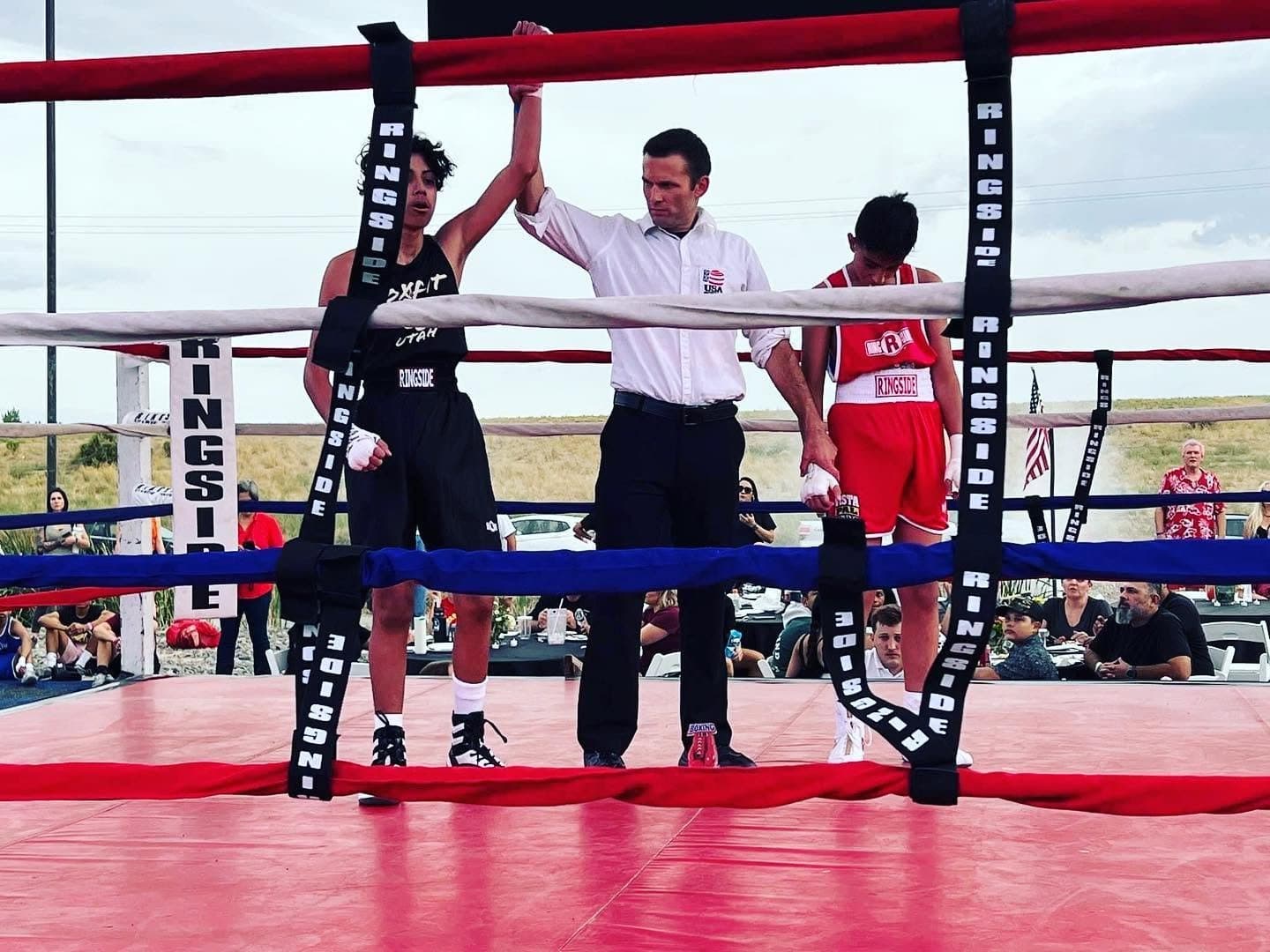 Referee raising a BoxFit Utah fighter's hand after a win in an outdoor ring